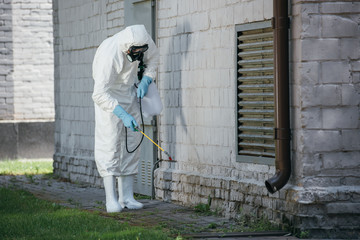 pest control worker spraying pesticides with sprayer on building wall