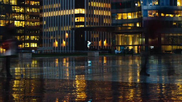Time lapse of crowd of people walking near modern buildings in Paris business district La Defense. Night city lights, illuminated windows of office center. Concept of big city, business, job, economy