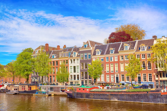 Cityscape view of the canal of Amsterdam in summer with a blue sky, house boats and traditional old houses. Picturesque of Amsterdam, North Holland, The Netherlands.