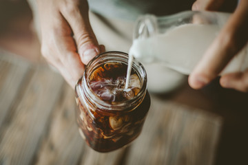 Man pouring milk in iced coffee