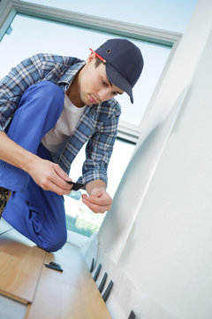 young worker in uniform installing new baseboard at home