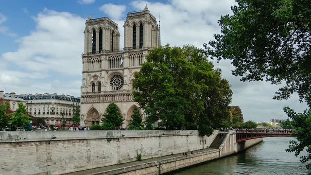Time lapse of ancient catholic cathedral Notre-Dame de Paris on summer cloudy day. Quays of the Seine river with boats. Water traffic, famous touristic places and popular travel destinations in Europe