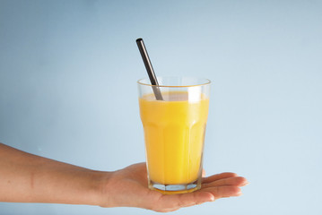 Hand holding glass of orange juice black straw isolated on blue background