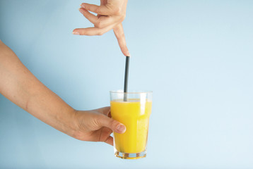 Hand holding glass of orange juice black straw isolated on blue background