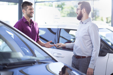 Professional car dealer giving keys to buyer in dealing salon