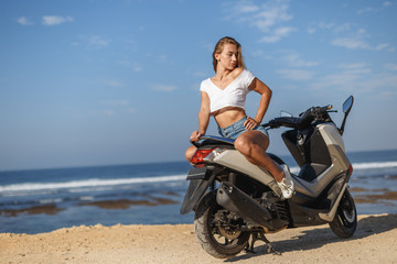 Fototapeta na wymiar Posing on scooter, young pretty sexy girl outdoor portrait near ocean in sports wear, jeans, freedom, scooter, bike