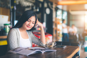 Beautiful attractive young Asian woman reading a magazine at cafe in the morning 
