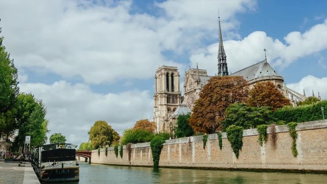 Time lapse of ancient catholic cathedral Notre-Dame de Paris on summer cloudy day. Quays of the Seine river with boats. Water traffic, famous touristic places and popular travel destinations in Europe
