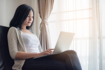 Beautiful attractive young Asian woman using laptop at living room in the morning 