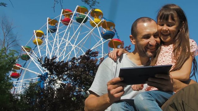 Happy family with a tablet. Happy daughter with father in the park with a gadget.