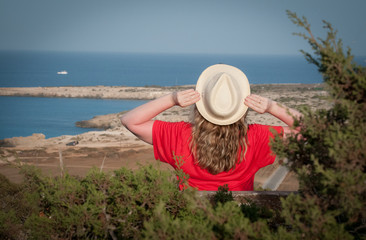 Fototapeta premium A girl in a hat looks at the sea. Cape Cave Greco, Cyprus, 2018
