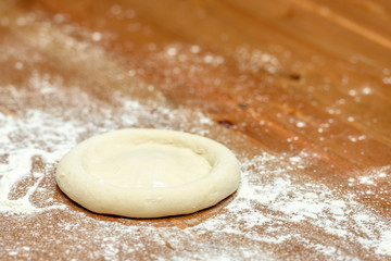 Pizza dough. Basis for baking pizza on a wooden table, close-up