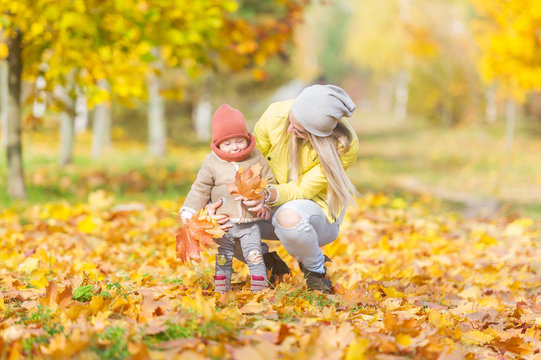 Happy mother and little daughter playing fun together in the autumn park.