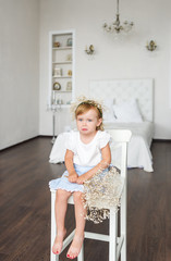 The little tetchy girl sits on a chair in the bedroom