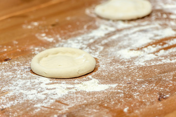 Pizza dough. Basis for baking pizza on a wooden table, close-up