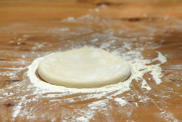 Pizza dough. Basis for baking pizza on a wooden table, close-up