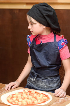 Little girl cook in uniform prepares pizza in the kitchen.