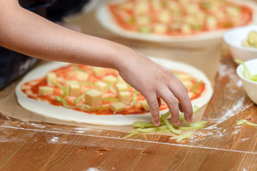 Close-up of children's hands preparing pizza. Children lay out on the basis of pizza vegetables and...