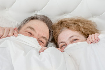 Happy senior couple lying under the blanket together. Top view