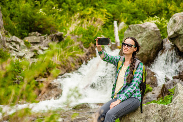 woman hiker taking selfie with smartphone near a waterfall