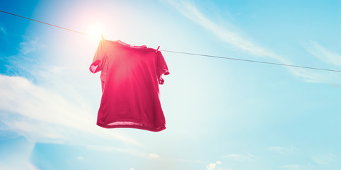 Red t-shirt on clothes line against sun and blue sky with clouds.