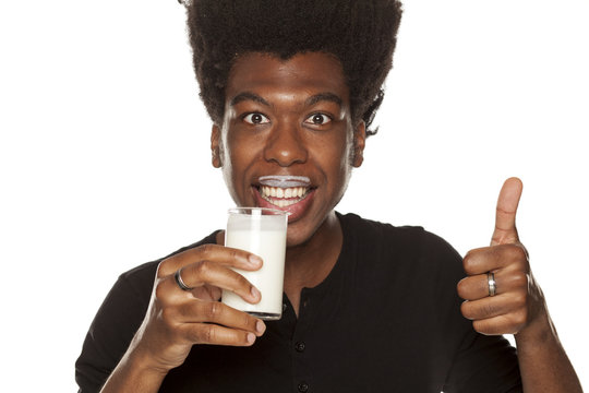 Portrait of young african american man drinking yogurt from a glass and showing thumbs up on white background
