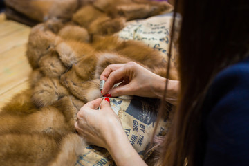 Professional tailor, designer repairing fur coat at atelier, studio. Fashion and tailoring concept