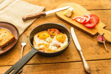 Rye scrambled eggs with onions and tomatoes in a frying pan on a rustic wooden background