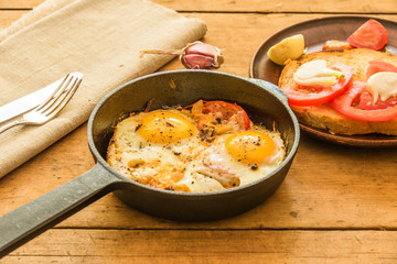 Rye scrambled eggs with onions and tomatoes in a frying pan on a rustic wooden background