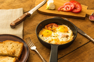 Rye scrambled eggs with onions and tomatoes in a frying pan on a rustic wooden background