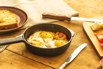 Rye scrambled eggs with onions and tomatoes in a frying pan on a rustic wooden background