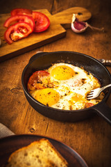 Fried eggs with tomatoes in a cast-iron frying pan on an old wooden table