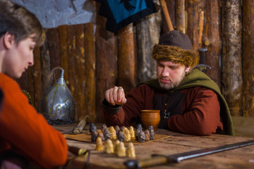 Two men in russian ethnic suit playing medieval popular strategy board game - tafl. Folk, competition and traditional concept