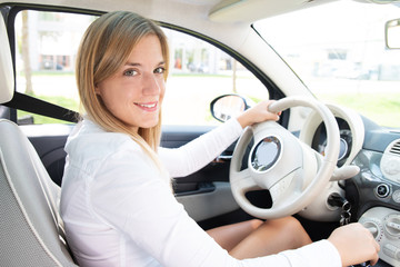 Junge Autofahrerin sympathisch lächelnd am Steuer ihres Wagens 