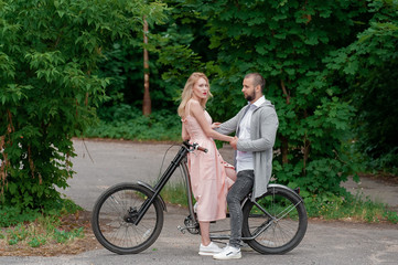 Obraz premium Close up of loving gentle couple riding on bike. People in love in park on sunset clodly time. Pretty girl with long hair and boy with bike. Time to kiss. Couple having a bicycles race into the nature