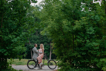 Close up of loving gentle couple riding on bike. People in love in park on sunset clodly time. Pretty girl with long hair and boy with bike. Time to kiss. Couple having a bicycles race into the nature