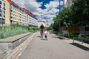 Young father on the bicycle with his 4 years old daughter on scooter 