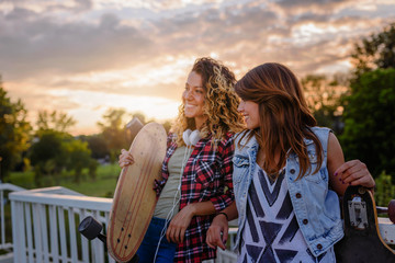 Smiling skate girls holding long-boards walking outdoors in the street having fun