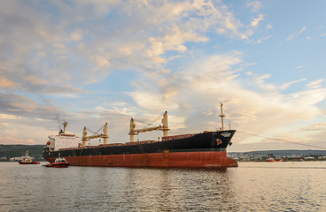 Fototapeta premium Tug boat entering the harbor with big cargo boat.