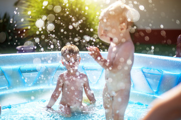 Baby kids playing at baby pool at backyard. Kids pool having fun. Summer day at home. Family time.
