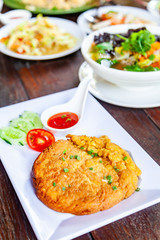Pork Omelet on White Plate with Som Tam and Many Food on Wood Table