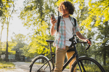 Attractive young happy male with curly hair looking on his mobile phone, choosing gps application...