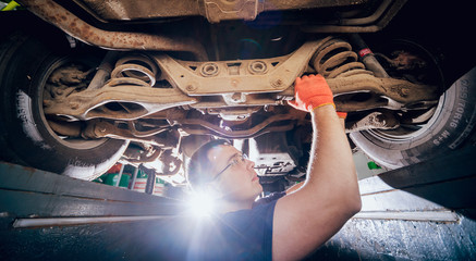 Car mechanic repair car suspension of lifted automobile at repair service station