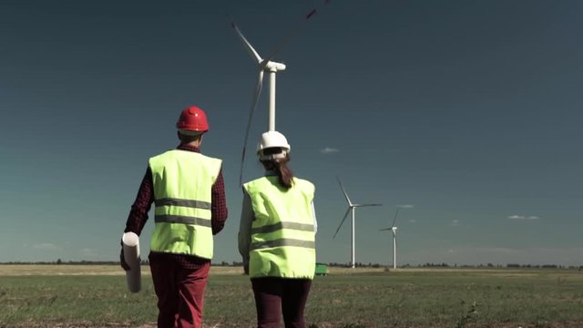 Two Successful Engineers Man And Woman Approach A Windmill And Discuss A Plan For The Construction Of A Similar Project. Alternative Energy Concept