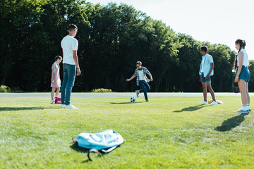 Obraz premium multiethnic teenage classmates playing with soccer ball in park