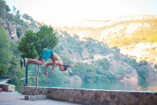 Young man doing a side flip or somersault while practicing parkour on a lake in the countryside.