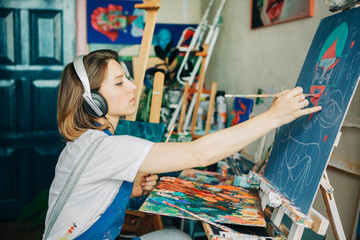 Young beautiful woman drawing something on  canvas and listening music,sitting  in art studio .
