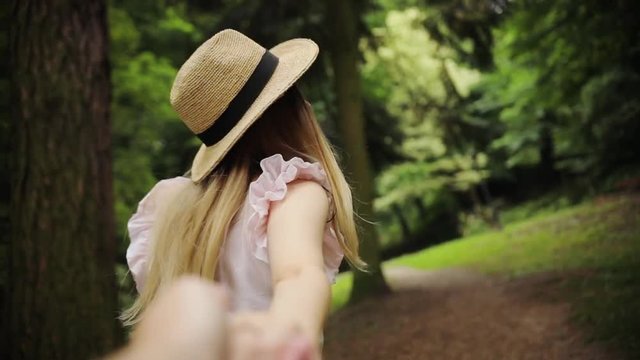Young woman with hat walking hold man hand look and pose at camera in park couple outside sun smile family behind crossingelegant road together view nature summer beauty enjoy slow motion