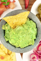 A closeup overhead photo of guacamole sauce in a molcajete, traditional Mexican mortar, with a nacho, tortilla chip