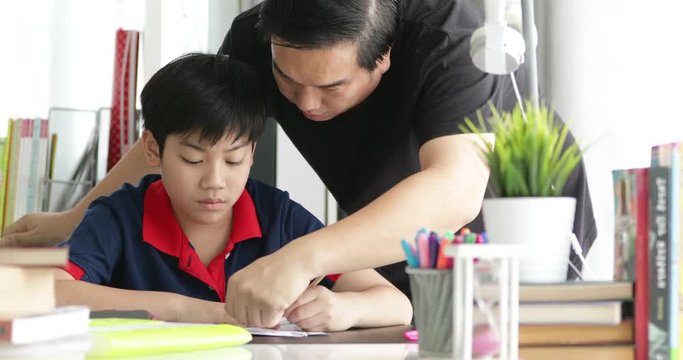 Asian Father and son doing homework on the table in the living room .